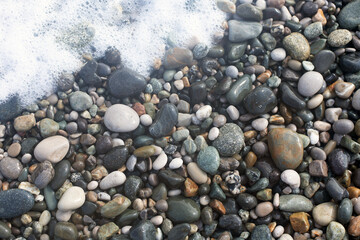 Wet smooth glossy sea shingle and white sea foam close up background in natural colors