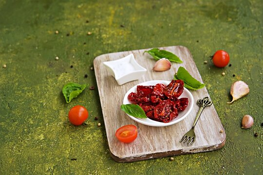 Homemade sun-dried tomatoes in a white bowl on a wooden board on an olive green concrete background. Canning, preserves. Harvest tomatoes.