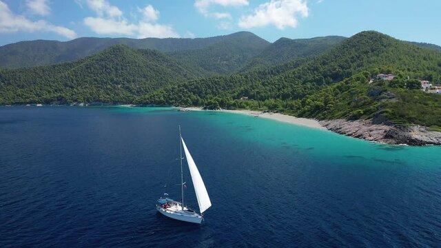Aerial drone video of sailing boat cruising near famous turquoise paradise beach of Milia covered with pine trees, Skopelos island, Sporades, Greece