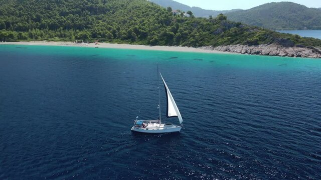 Aerial drone video of sailing boat cruising near famous turquoise paradise beach of Milia covered with pine trees, Skopelos island, Sporades, Greece