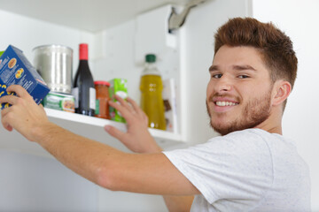 young man putting food away in the cupboard