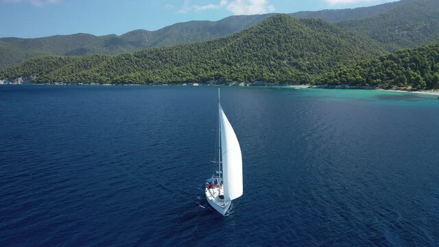 Aerial drone video of sailing boat cruising near famous turquoise paradise beach of Milia covered with pine trees, Skopelos island, Sporades, Greece