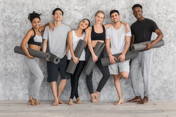 Fototapeta na wymiar Fitness Class. Sporty multiethnic people with yoga mats posing near gray wall