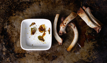 Leftovers from a rib dinner, bones and empty side dish of brussels sprouts, on a metal tray.