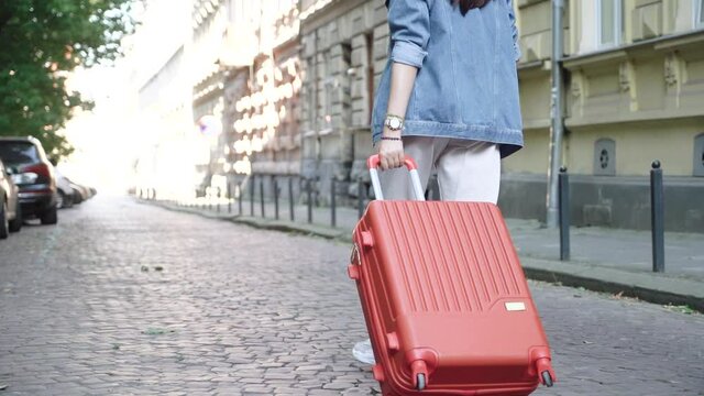 Girl in white jeans walks through the old city with an orange luggage suitcase. Travel through the old European city