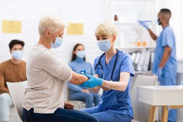Fototapeta premium Senior Woman Receiving Coronavirus Vaccine Injection Sitting With Doctor Indoor