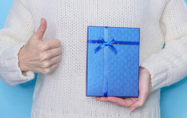 person holding a gift box
A woman in a white sweater holds a blue gift box in her hand and shows a cool close-up side view.