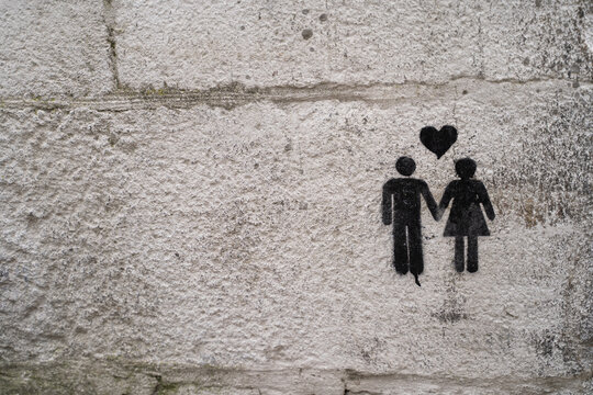 Street graffiti of a man and a woman holding hands with a heart in the middle. A couple in a wall.