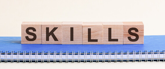 SKILLS - a word made of wooden blocks with black letters, a row of blocks is located on a blue Notepad.