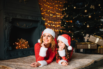 Merry Christmas and Happy Holidays! Beautiful mother with little daughter in Christmas costumes spend time together near the Christmas tree.