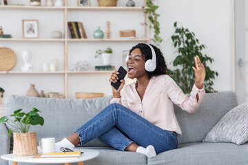 Fototapeta premium African Lady Listening Music And Singing At Home, Using Smartphone As Microphone