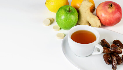 Fruit tea cup, dates on the white saucer. Tropical citrus fruits, ginger  and multivitamins pills on the white background. Autumn, seasonal relaxing concept.