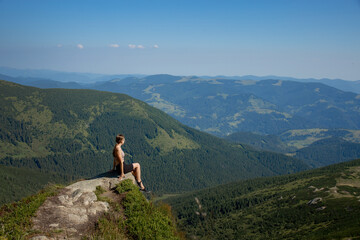 Naklejka na ściany i meble A girl sits on the edge of the cliff and looking at the sun valley and mountains