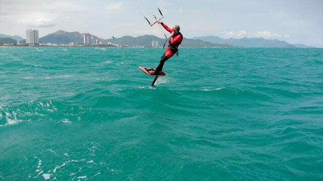 Athlete showing sport trick jumping with kite and board in air. Extreme water sport and summer vacations concept. Acrobatic jump of professional kite surfer on the sea wave.