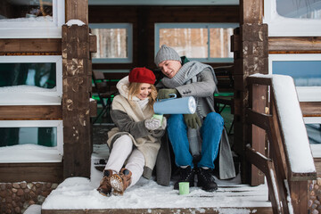 After spending a day off in the woods in winter, a young couple basks in a summer house and drinks a hot drink from mugs.