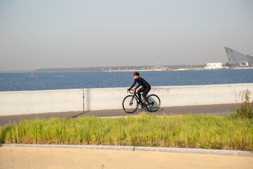 Obraz premium A woman rides a bicycle along the embankment. Riding a bicycle. Outdoor sports. Embankment of the Gulf of Finland Russia St. Petersburg.Cycling workout