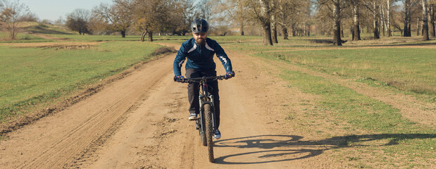 Fototapeta premium Cyclist in pants and fleece jacket on a modern carbon hardtail bike with an air suspension fork rides off-road. The guy is resting on a bench in the autumn park.