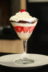 A bowl with a strawberry dessert with cherry, whipped cream and chocolate