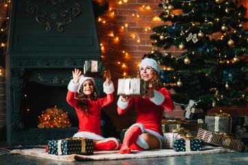 Merry Christmas and Happy Holidays! Cheerful mom and her cute daughter girl in Christmas costumes exchanging gifts.