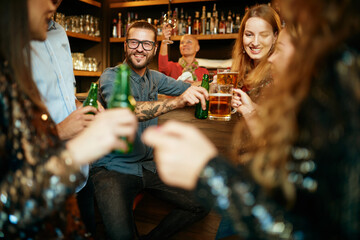 Group of best friends sitting in a pub, chatting and toasting with beer.