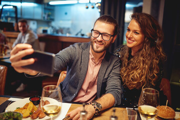 Attractive hipster couple sitting in a restaurant and taking a selfie. It's a diner time.
