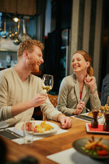 Cheerful friends sitting in restaurant for dinner, eating and drinking wine.