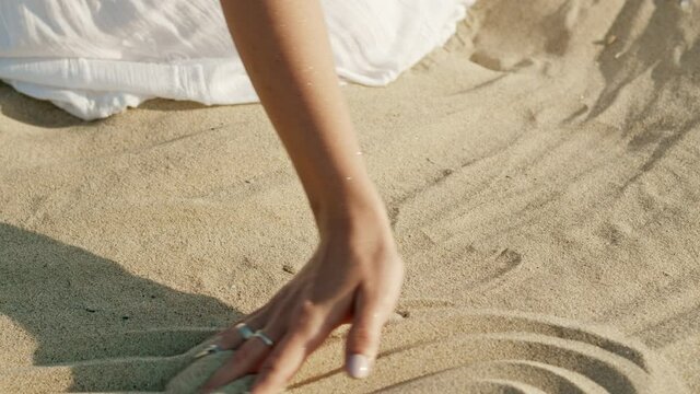 Woman hands playing with sand at beach. Beautiful scene of young boho gypsy girl in white dress with rings touching grit. Slow motion