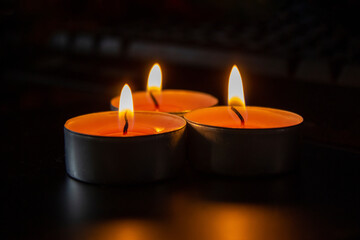 Composition of three candles on dark luxury night background. Black table, side view. Candles Burning at Night. Orange taper burning in focus, foreground. illustration design.