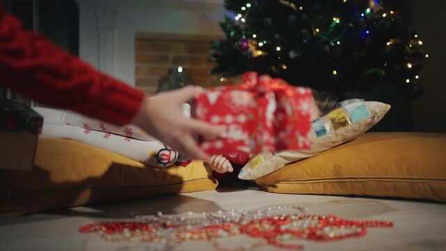 A small child is sleeping next to christmas tree. Christmas presents appear secretly.