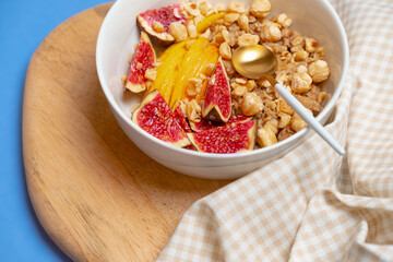 Porridge with figs, apple, nuts and napkin on wooden desk and blue backdrop. English homemade breakfast. Granola with fruits. Healthy nutrition and lifestyle. Close up