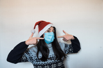 Una chica joven con un gorro de navidad apunta a su mascarilla quirúrgica