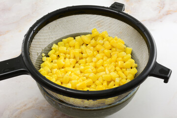 Freshly rinsed canned corn kernels draining in strainer in bowl on table