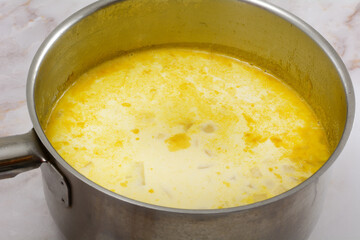 Making chowder soup with milk and chopped potatoes and mirepoix base in stainless steel cooking pot
