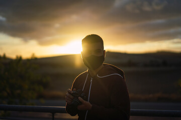 Fototapeta premium Chico joven con mascarilla negra con el atardecer de fondo