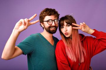 Positive studio portrait of crazy young hipster couple having fun together, showing peace gesture...