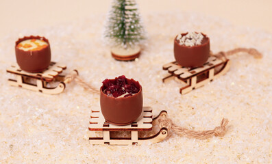 chocolates on a sled
Three chocolates lie on a sled in the snow with a Christmas tree in the back, close-up side view.