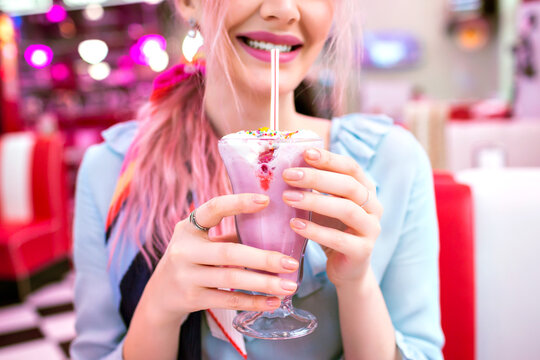 Close up image of woman holding sweet strawberry milk shake, pin up retro style, pastel colors, vintage American cafe.
