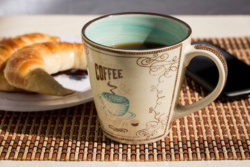 Picture of a cup of coffee, a plate with croissants and a mobile phone