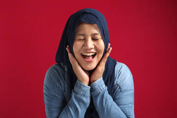 Portrait of beautiful Asian muslim woman wearing blue hijab smiling at camera, hands under chin