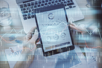 Double exposure of man's hands holding and using a digital device and forex graph drawing. Financial market concept.