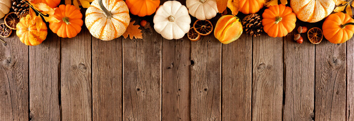 Long fall border of pumpkins and natural autumn decor. Top view on a rustic dark wood banner...