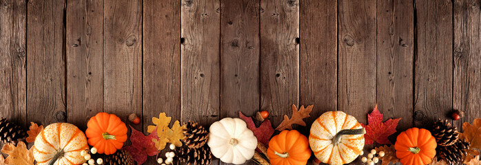 Natural fall border with pumpkins and leaves. Top down view on a rustic dark wood banner background with copy space.