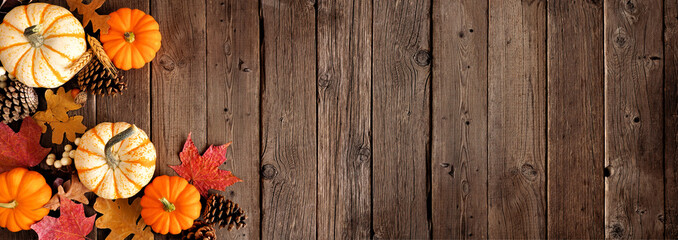 Natural autumn corner border of pumpkins and leaves. Overhead view on a rustic dark wood banner background with copy space.