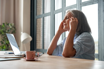 Stressed overworked old mature business woman suffering from headache at work. Tired sick senior...