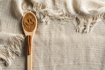 Ground cinnamon in a wooden spoon with a happy face and a stick on a fabric tablecloth with fringe...