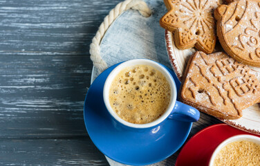 Homemade gingerbread cookies and red and blue cups with coffee on tray on grunge gray wooden background. Christmas and New Year celebration background. Close up of home baked cookies with icing.