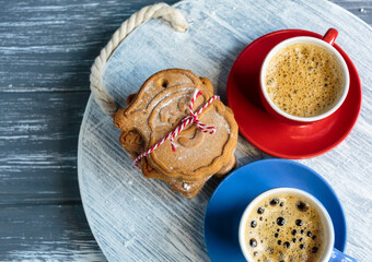 Homemade gingerbread cookies and red and blue cups with coffee on tray on grunge gray wooden background. Christmas and New Year celebration background. Close up of home baked cookies with icing.
