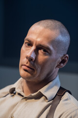 Bald investigator tired after questioning, portrait. A brutal man with a gun holster in a dark room...