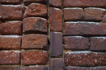 Photo of the exterior surface of an ancient brick wall. Abundant traces of time on the red brick and in the destroyed layer of mortar. In dark red tones.