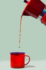 Cafeteira derramando o café na xícara vermelha com fundo verde.